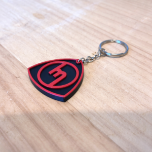 Red and black Mazda old-school logo keyring on a timber surface